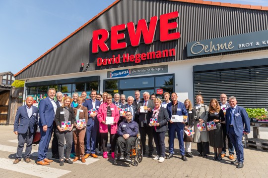 Auf dem Bild ist eine Gruppe von etwa 30 Leuten vor einem REWE Markt zu sehen.