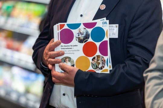 Auf dem Bild ist ein Oberkörper zu sehen, vor dem in beiden Händen Ausgaben der Broschüre „Ein Gewinn für jedes Unternehmen – Arbeits- und Fachkräfte mit Behinderung“ der G.I.B. gehalten werden.