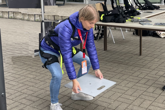 Auf dem Bild ist eine Frau zu sehen, die ein Exoskelett trägt und damit eine große Steinplatte vom Boden aufhebt.