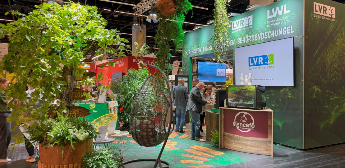 Das Bild zeigt den Messestand unter dem Motto des Behördendcshungels mit vielen Pflanzen und einem Cafe.