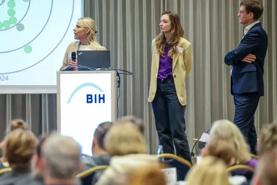 Das Bild zeigt drei Personen aus dem Forschungsprojekt während eines Vortrags.