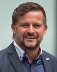 Potrait von Herrn Wagner: Er hat kurze braune Haare, einen kurzen Bart und trägt ein graues Jacket.